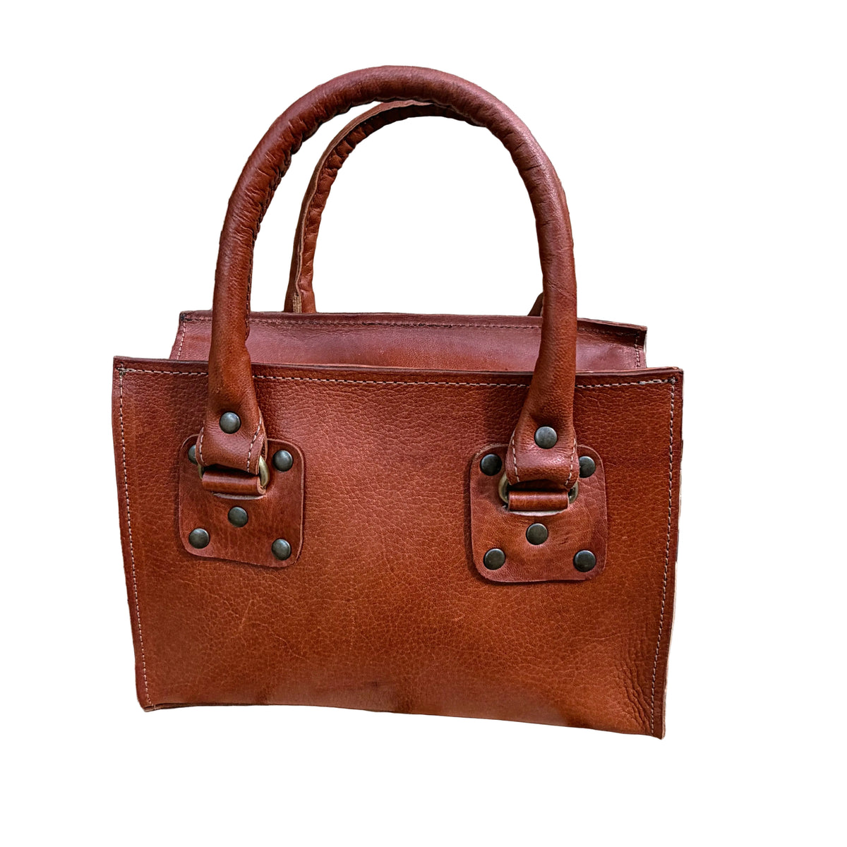 A brown leather handbag with double top handles and metal hardware, displayed on a rustic wooden table in front of a large woven basket.