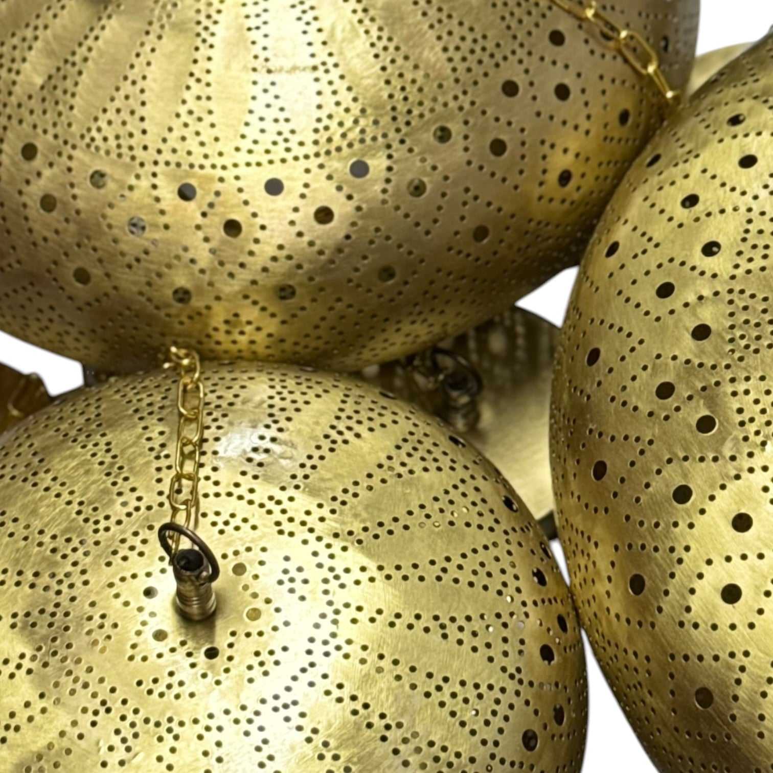 Close-up of gold spherical objects with perforated design and chain attachments.