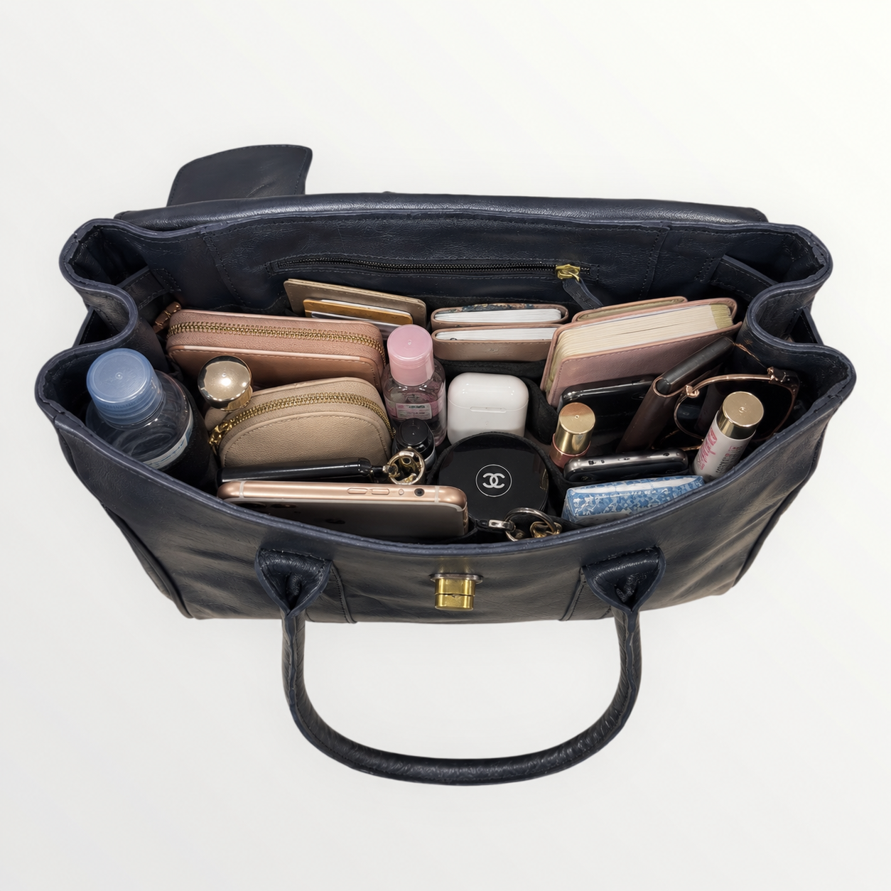 Black handbag with various cosmetic items on a white background